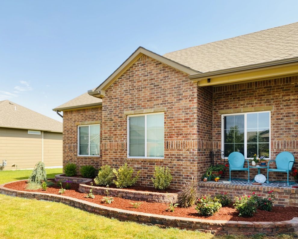 Two-tier stone retaining wall beds along the front of a brick home