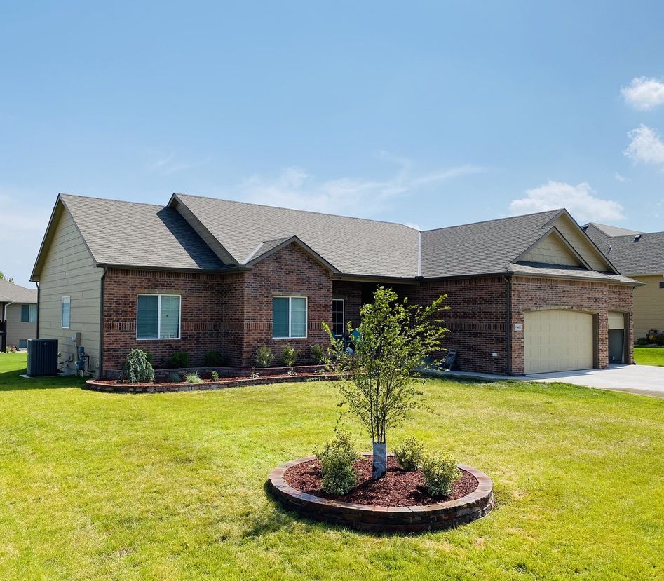 Brick home with landscaped front beds along the house and a round stone tree bed in the lawn