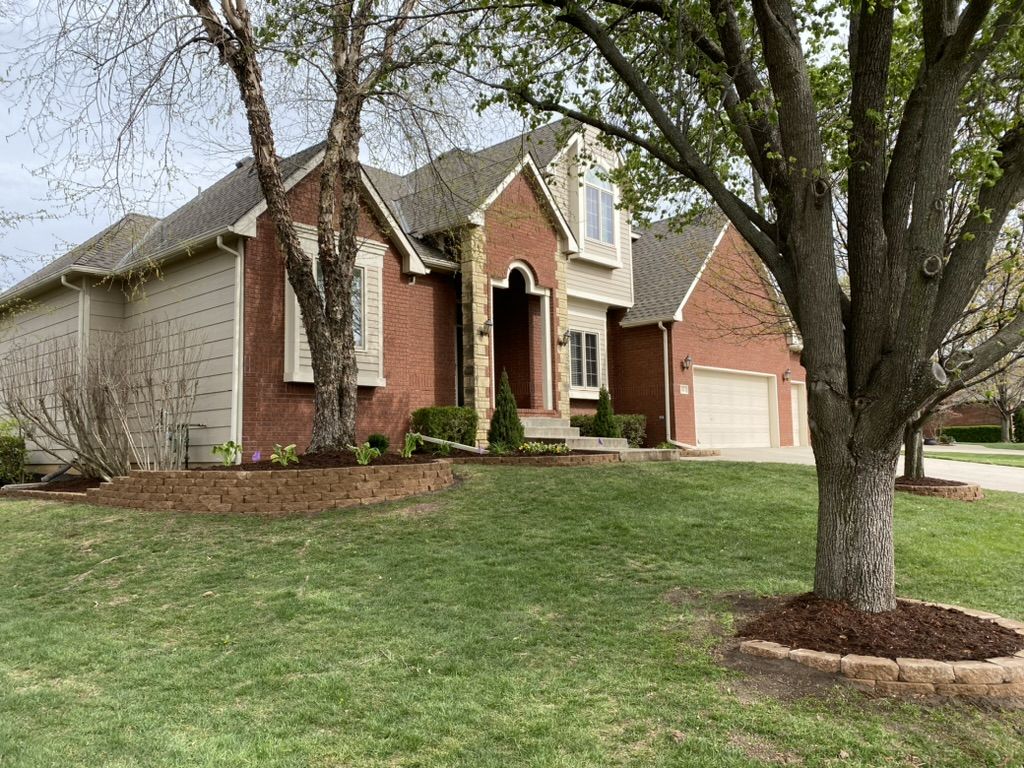 Corner view of the front beds and a stone ring around a large tree